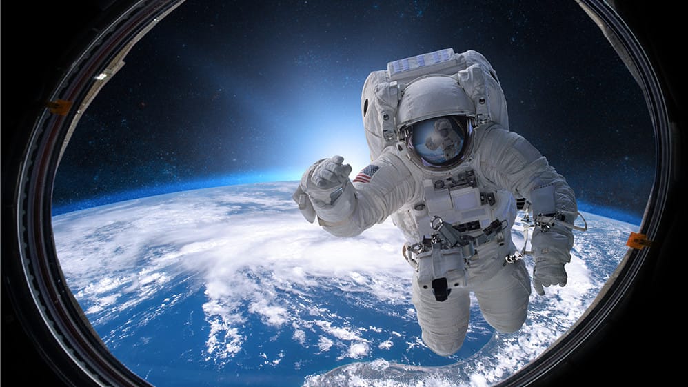 Astronauta flutuando no espaço visto através da janela da ISS, com o planeta Terra e o universo ao fundo — representação da astronomia na exploração espacial.