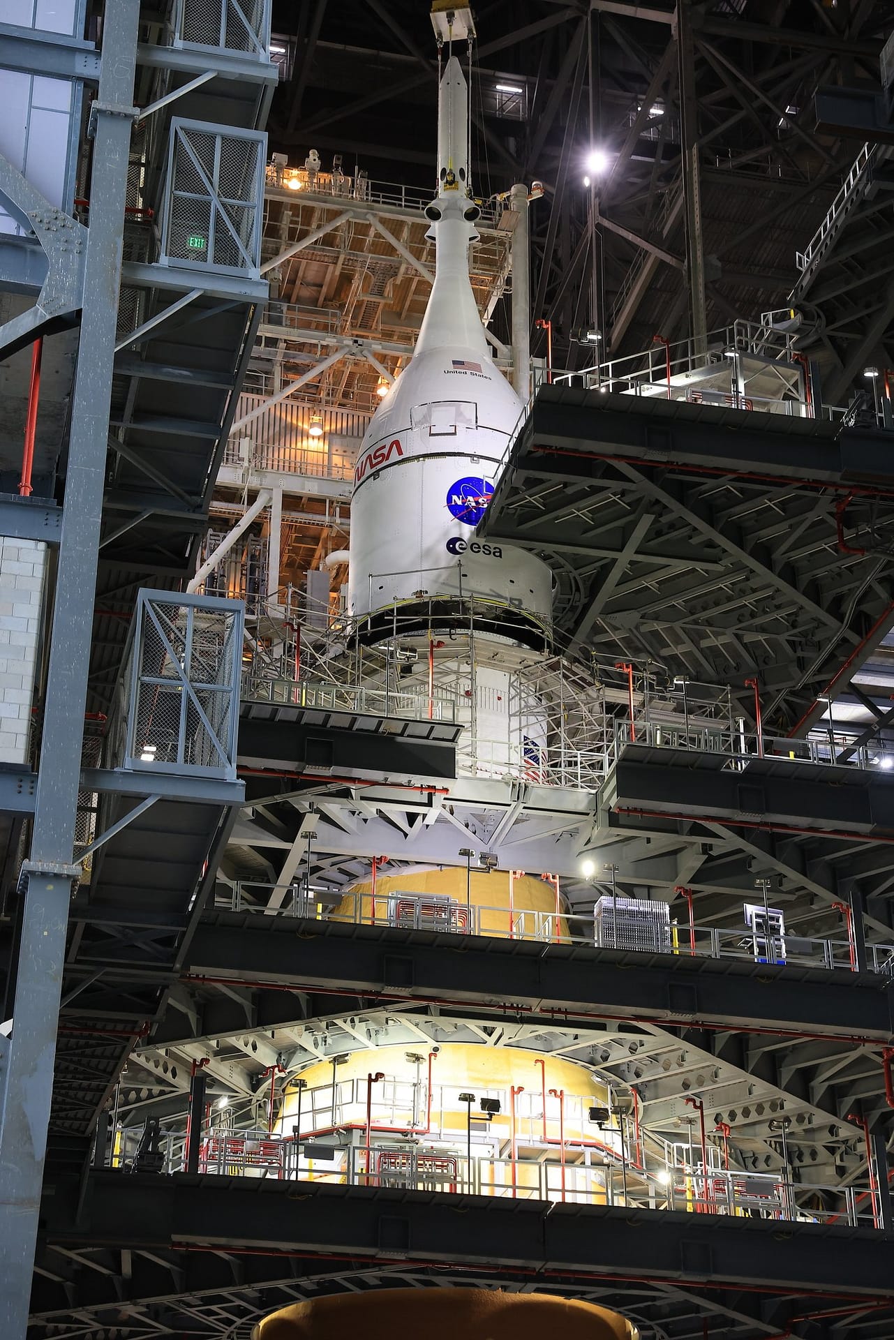 Vista de longe da nave Orion sendo elevada pelo guindaste no local de lançamento, durante o processo de montagem no foguete SLS para a missão Artemis 2. Créditos: NASA