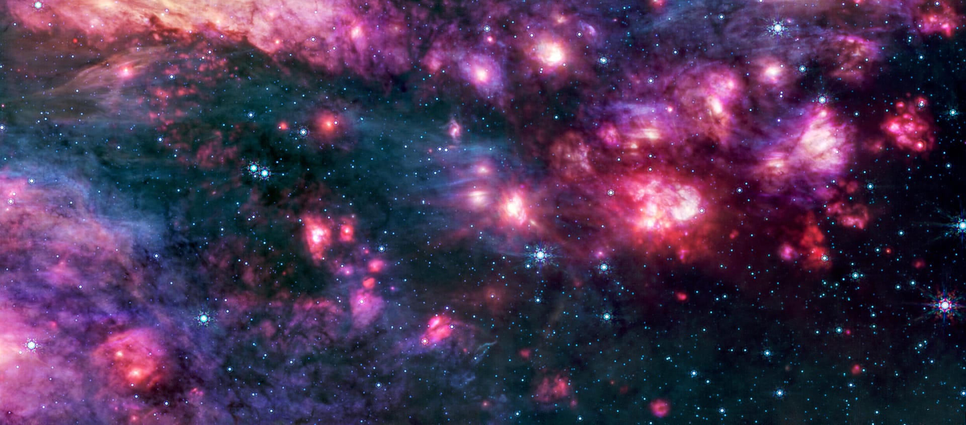 Nuvens cósmicas em tons de rosa e roxo, algumas com centros brilhantes, estão cercadas por áreas escuras que se assemelham ao espaço negro pontilhado por estrelas azul-azuladas. Um grupo de pequenas nuvens à direita é mais avermelhado do que qualquer outra região da imagem.