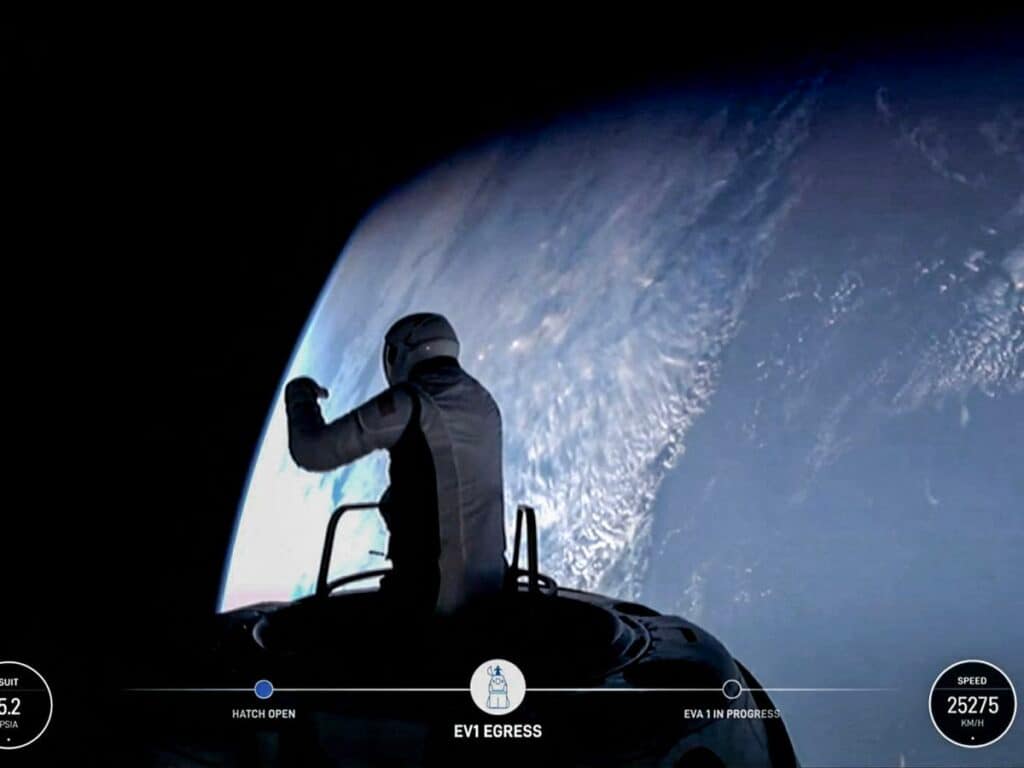 O empresário Jared Isaacman durante sua caminhada histórica no espaço, fora da cápsula, preso a um equipamento de segurança. Ele está usando um traje espacial completo, e é possível ver a curvatura da Terra ao fundo, com o vasto espaço ao redor e o traje refletindo a luz do ambiente. A missão é parte da 'polaris Dawn'