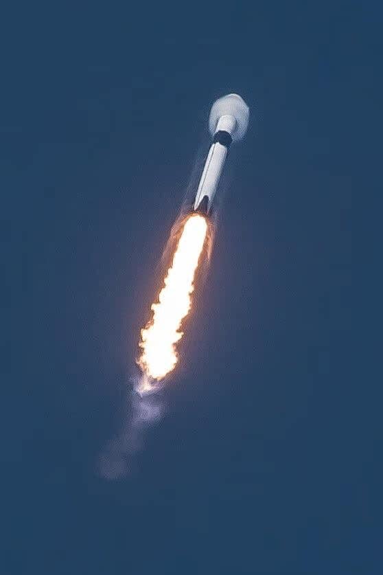 Foguete Falcon 9 quebrando a barreira do som, com os motores Merlin emitindo uma grande coluna de chamas. A imagem mostra claramente o cone de choque formado pela velocidade supersônica, com uma potente aceleração
