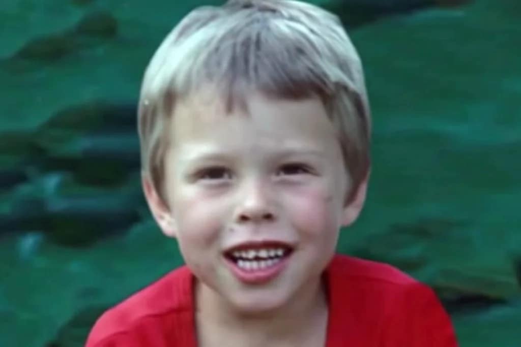 Elon Musk quando criança, vestindo uma camiseta vermelha, com sorriso tímido e dentes ainda em formação.